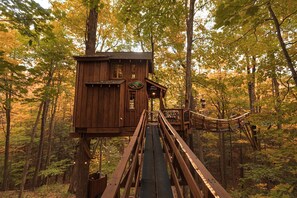 A wooden treehouse with a wooden staircase leading up to it, surrounded by a forest. - Magical Tree House Rental in the Woods near Syracuse for Glamping in New York State (Lafayette)