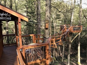 A wooden deck with a 'WELCOME' sign, a wooden bridge, and a treehouse structure in a forest setting. - Magical Tree House Rental in the Woods near Syracuse for Glamping in New York State (Lafayette)
