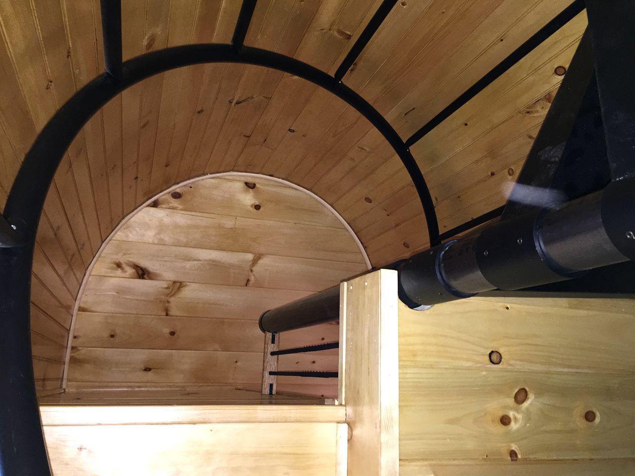 A wooden ceiling with a curved arch and a black pipe running through it.