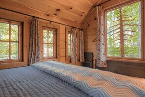 A wooden cabin room with a bed, large windows, and a fireplace.
