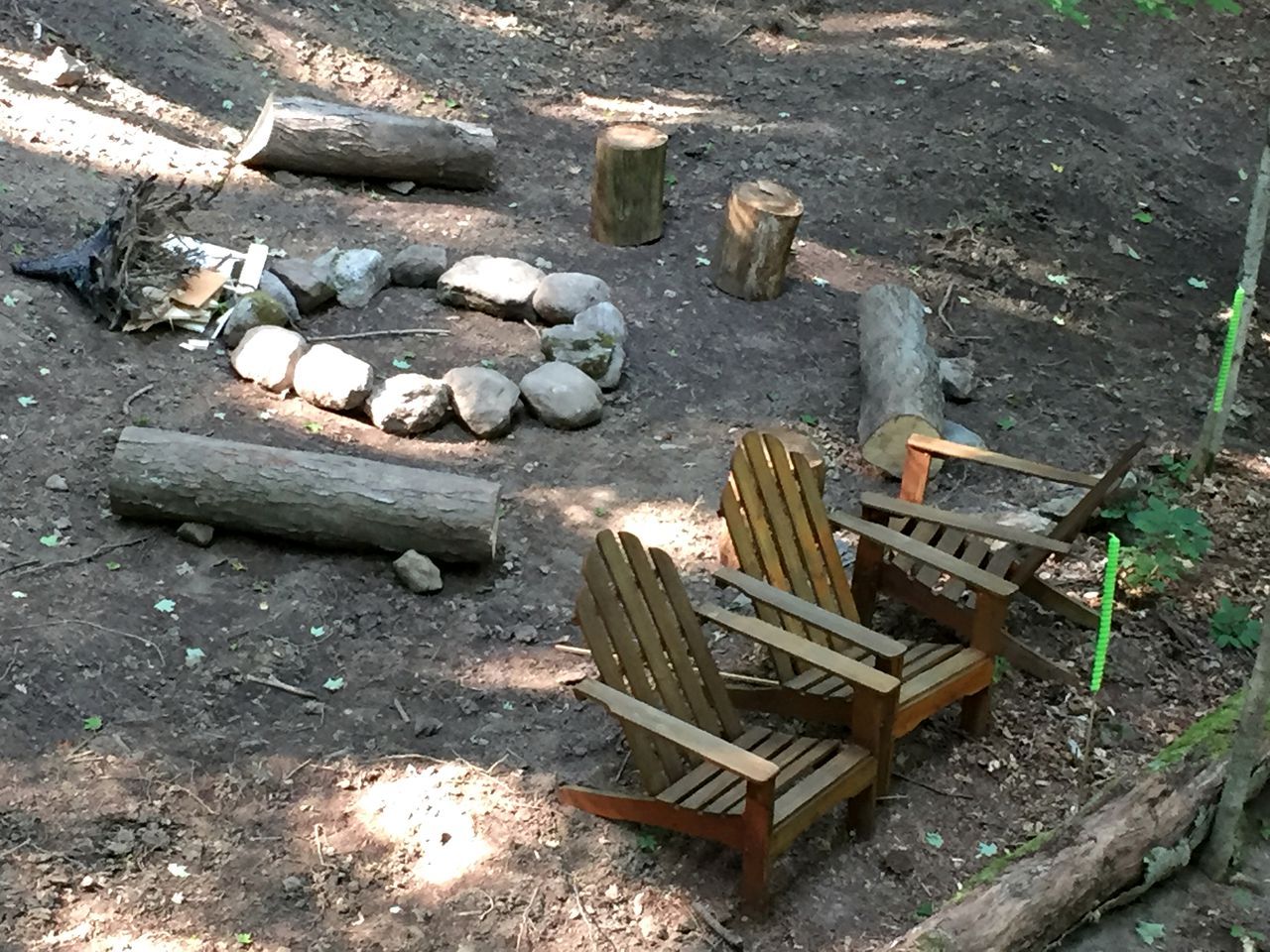 Une zone boisée avec un foyer, des bûches, des rochers et des chaises en bois.