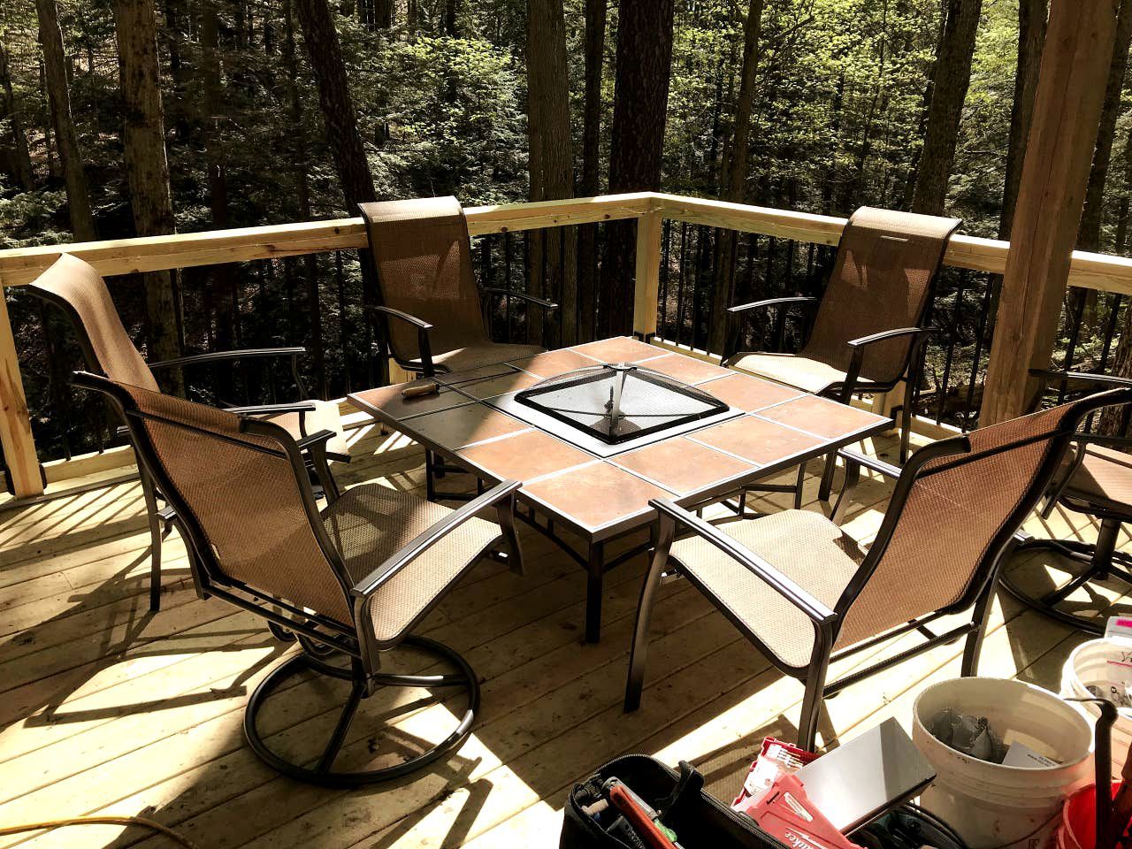 Una terraza de madera con una mesa y sillas, rodeada de árboles.