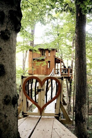 A wooden treehouse with a heart-shaped gate, surrounded by trees.