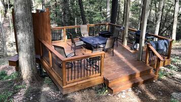 Una terraza de madera con mobiliario exterior, rodeada de árboles.