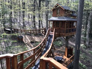 A wooden treehouse with a slide, surrounded by a forest. - Magical Tree House Rental in the Woods near Syracuse for Glamping in New York State (Lafayette)