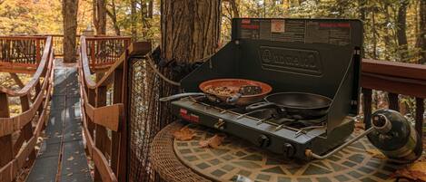 A propane stove set up on a wooden platform surrounded by trees.