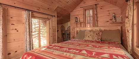 A wooden cabin bedroom with a bed, curtains, and a window.