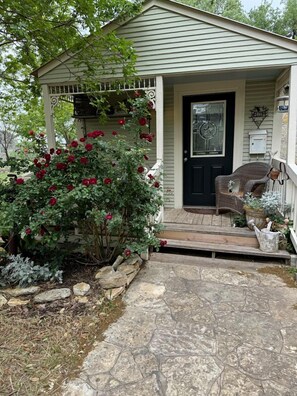 A house with a porch, a black door, and a small garden with red roses.