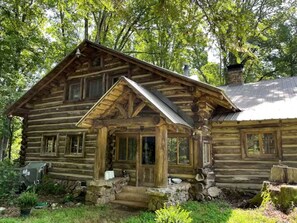 Une cabane rustique en rondins de bois, dotée d’un porche, d’une cheminée et de fondations en pierre.