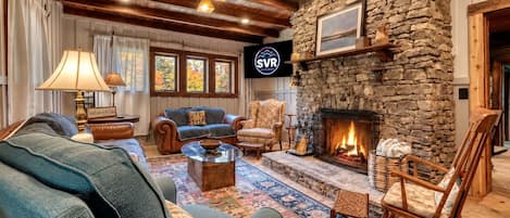 Ein gemütliches Wohnzimmer mit Kamin aus Stein, bequemen Sitzmöglichkeiten und einem Fernseher, der das SVR-Logo zeigt.