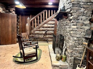 Un intérieur rustique avec un fauteuil à bascule en bois, une cheminée en pierre et un escalier en bois.