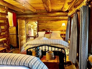 Een kamer in de stijl van een blokhut, met een bed, een tafeltje met een lamp en een geruit gordijn.