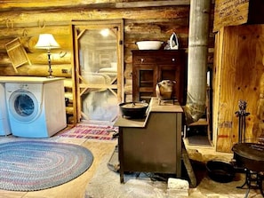 L’intérieur d’un chalet rustique, où l’on peut voir une machine à laver, un poêle et un lit.
