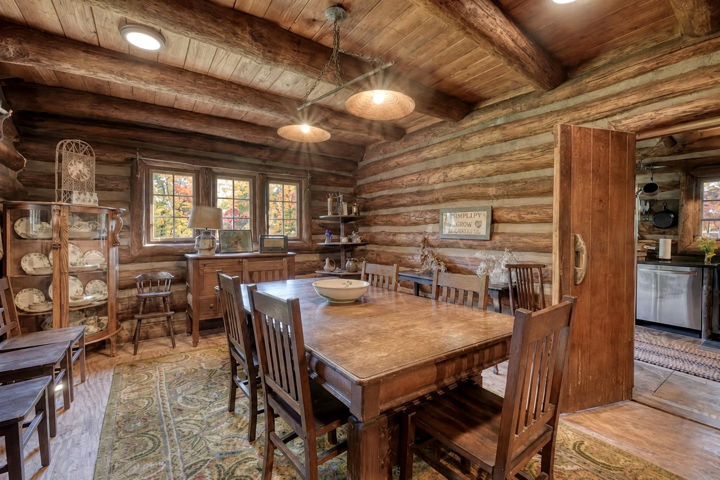 L’intérieur d’un chalet rustique comprend une table à manger en bois, des chaises, un lustre et un coin cuisine.