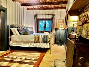 Une pièce avec un lit, une fenêtre avec des rideaux, une lampe et un mur en pierre.