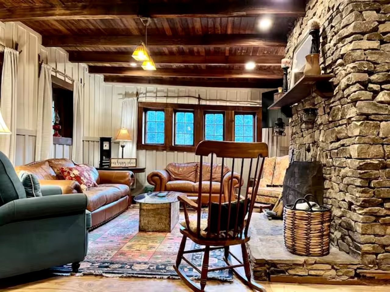 Una sala de estar acogedora con chimenea de piedra, vigas de madera en el techo y un amplio ventanal de múltiples cristales.