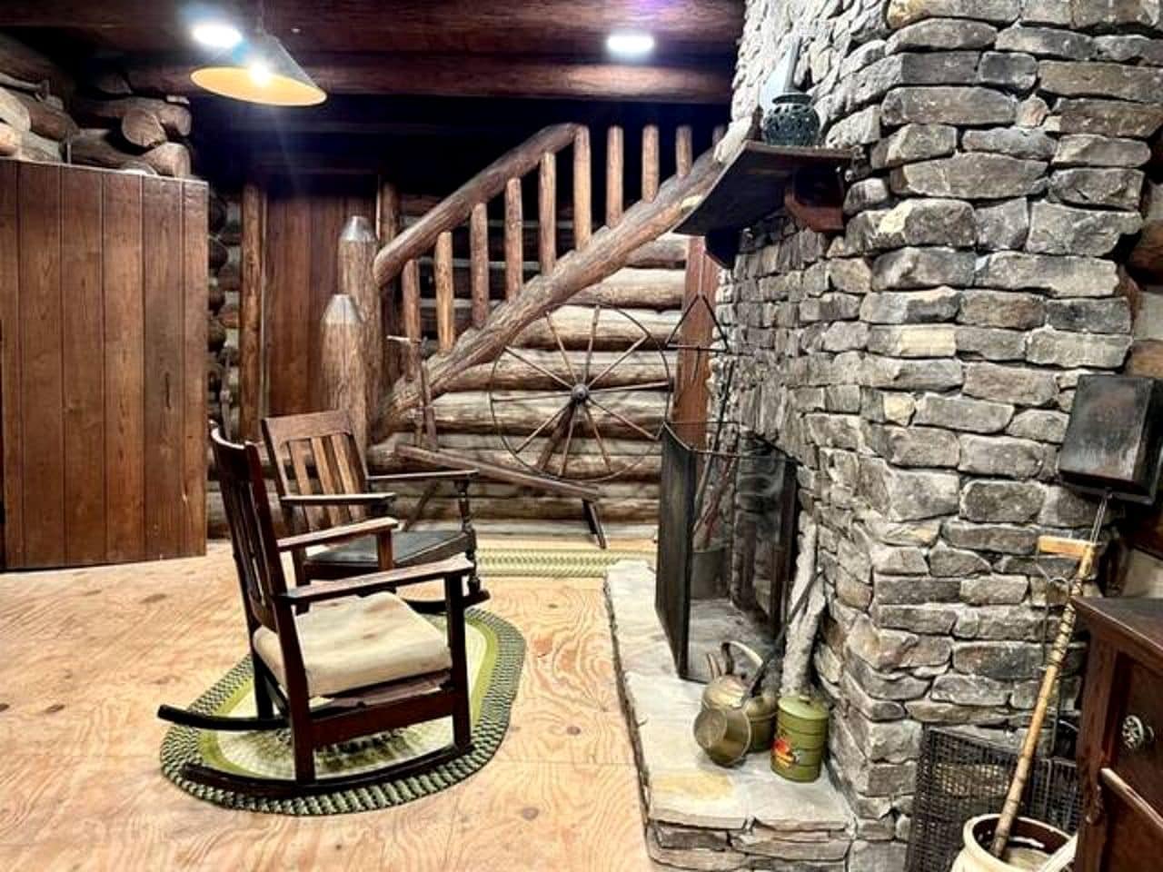 A rustic interior with a wooden rocking chair, stone fireplace, and a wooden staircase.