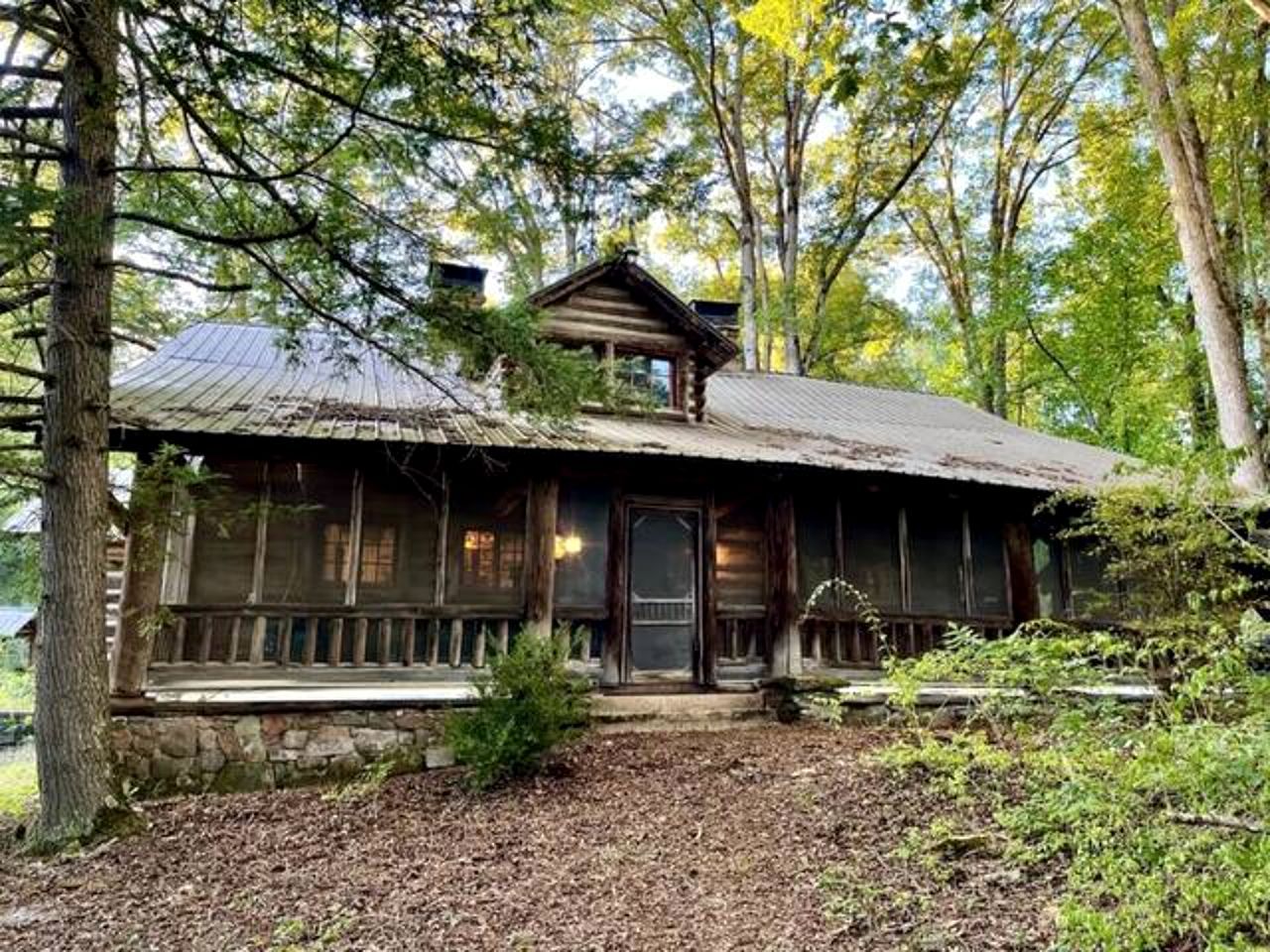 A rustic cabin with a stone foundation, wooden exterior, and a porch with a railing.