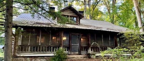 A rustic cabin with a stone foundation, wooden exterior, and a porch with a railing.