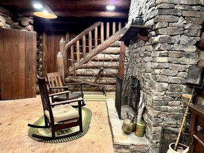 Ein rustikales Interieur mit einem Schaukelstuhl aus Holz, einem Kamin aus Stein und einer Holztreppe.