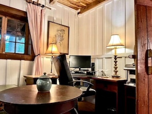 Une pièce avec une table en bois, une chaise, un bureau avec un ordinateur, une lampe et une fenêtre avec des rideaux.