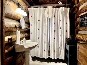 Een rustieke badkamer met een houten wand, een wit wastafel, een spiegel en een douchegordijn met bloemenprint.