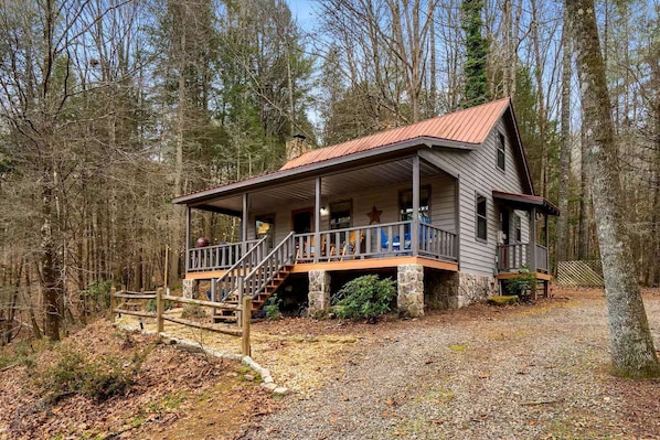 A cabin with a porch, stone foundation, and a metal roof.