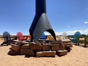 A large, dark-colored structure with a conical top, surrounded by colorful Adirondack chairs and a stack of stones. - Traditional Navajo Hut Rental for a Secluded Vacation near Page, Arizona (Page)