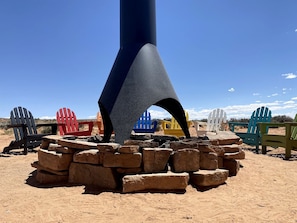 A large, dark-colored structure with a conical top, surrounded by colorful Adirondack chairs and a stack of stones. - Traditional Navajo Hut Rental for a Secluded Vacation near Page, Arizona (Page)