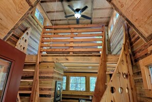 A wooden interior with a slatted ceiling, large windows, and a ceiling fan.