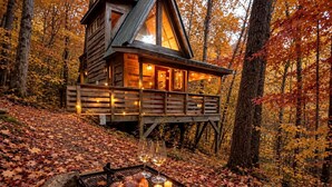A cabin with a deck, surrounded by autumn leaves, with a table set for a meal. - Charming Tree House with a Hot Tub in Chattahoochee National Forest, Georgia (Suches)