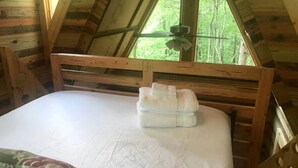 Een kamer met houten frame, een bed, een plafondventilator en een raam met uitzicht op bomen.