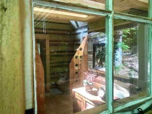 A rustic cabin interior with a wooden staircase, a small table with a vase, and a window overlooking a forest.