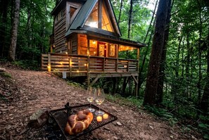 A wooden cabin with a deck, surrounded by forest.