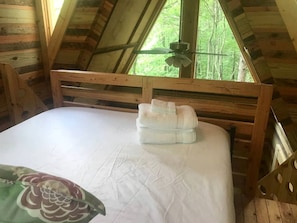 A wooden-framed room with a bed, a ceiling fan, and a window with a view of trees. - Charming Tree House with a Hot Tub in Chattahoochee National Forest, Georgia (Suches)