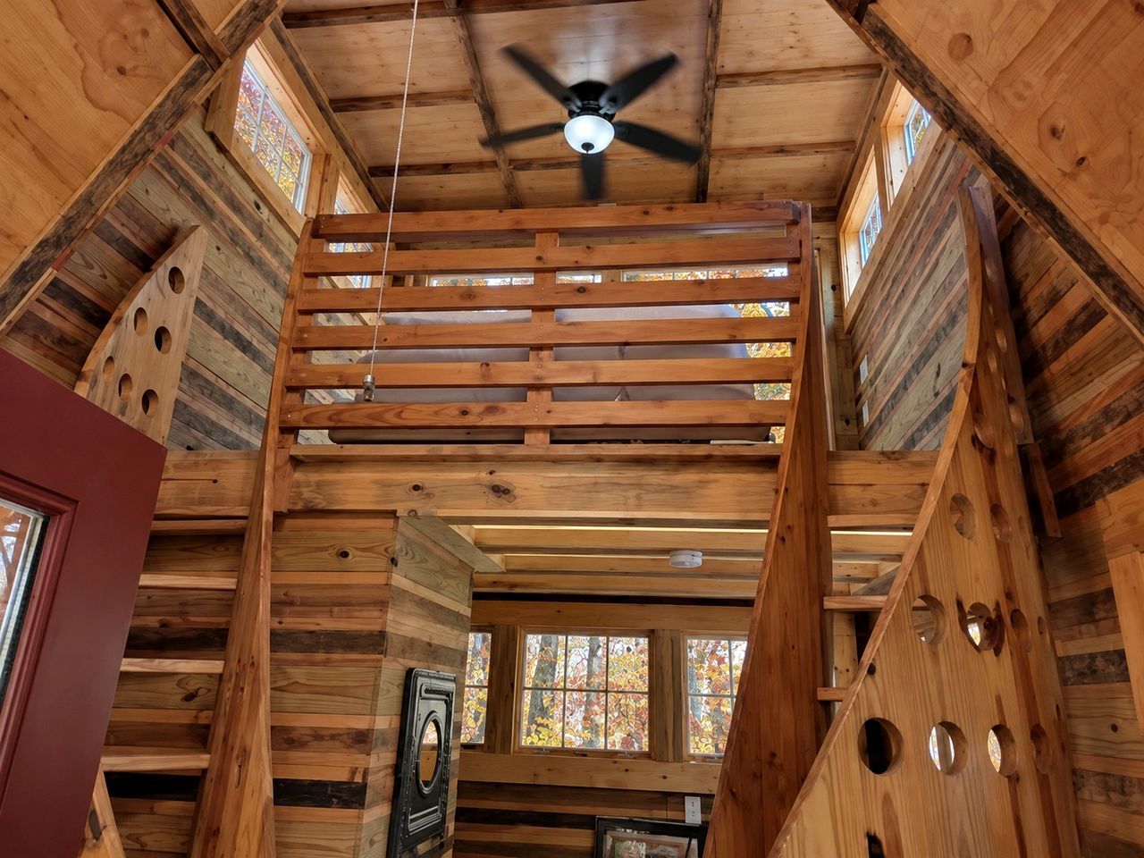 A wooden interior with a ceiling fan, wooden beams, and a window with stained glass.