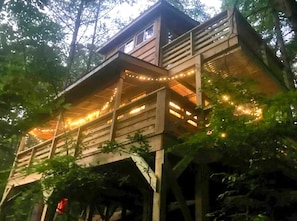 A wooden treehouse with multiple levels, string lights, and a view of the surrounding forest. - Charming Tree House with a Hot Tub in Chattahoochee National Forest, Georgia (Suches)