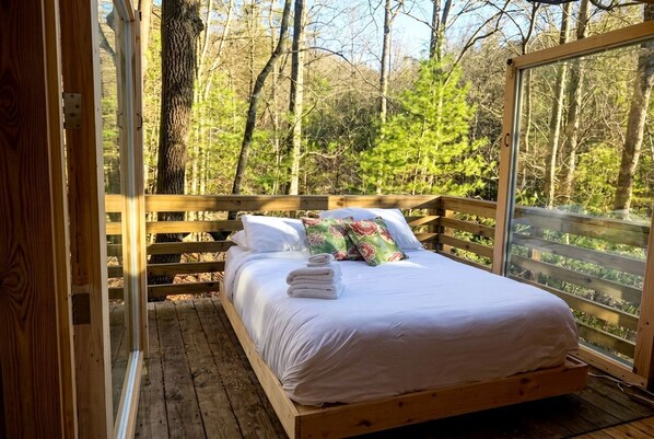 A wooden bed in a room with a view of a forest.