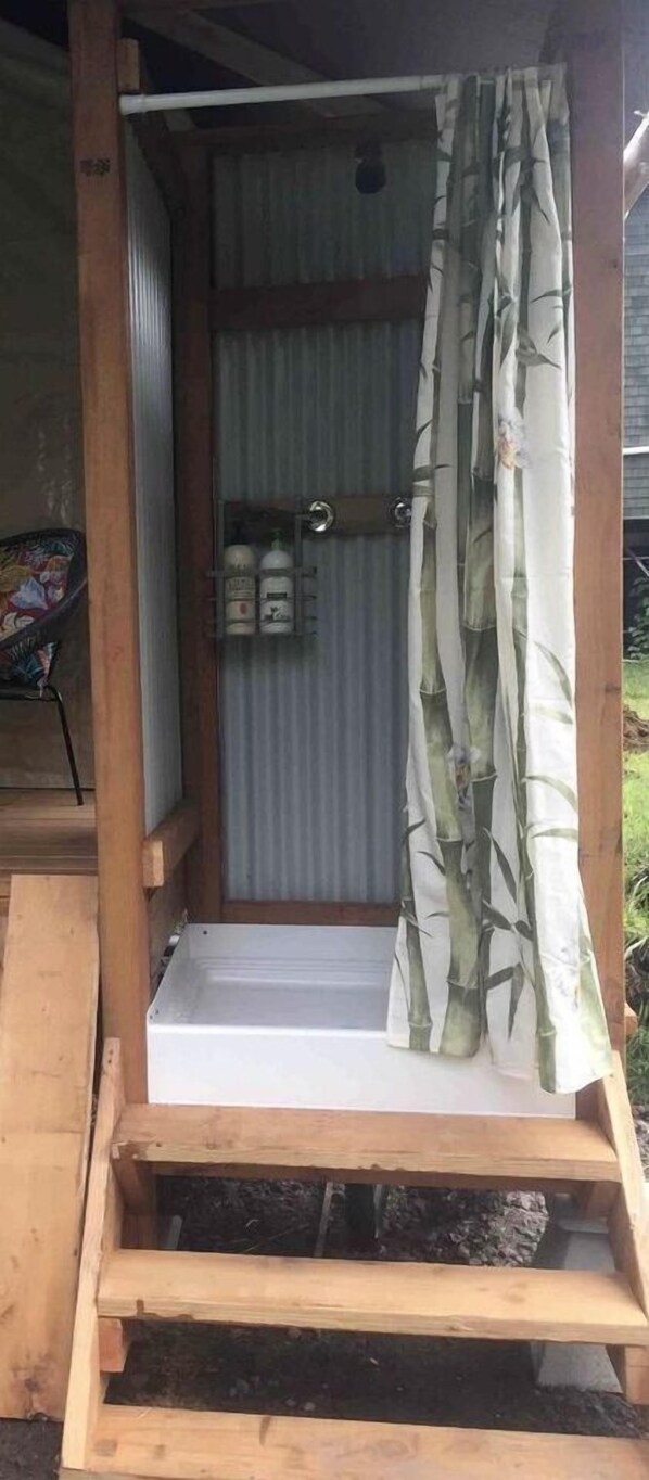 Eine Holzhütte mit einer Metalttür, einem Vorhang mit Bambusmuster und einem kleinen Regal mit Flaschen.