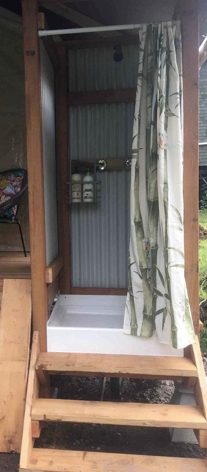Une structure en bois avec une porte en métal, un rideau à motifs de bambou et une petite étagère avec des bouteilles.