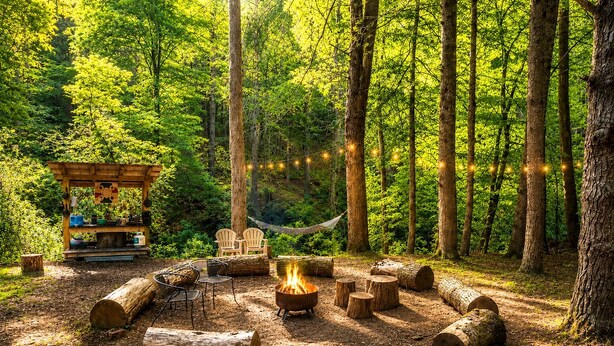A forested area with a fire pit, seating, and a small wooden structure with chairs. - Wonderful Tree House Getaway on the Toccoa River, for Glamping in Suches, Georgia (Suches)