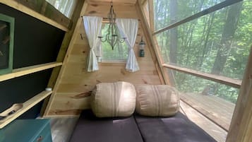 A cozy, triangular wooden cabin with a bed, pillows, and a chandelier.