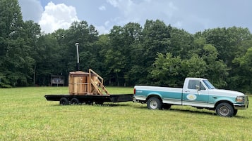 Een pickup truck trekt een houten constructie over een grasveld, met bomen op de achtergrond.