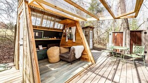 A wooden cabin with a loft bedroom, a dining area with outdoor seating, and a small shed in a wooded setting. - Off-Grid Experience in Cozy Mini A-Frame in Picturesque Tennessee (Grandview)
