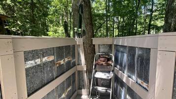Una terraza de madera con una escalera metálica, rodeada de árboles.