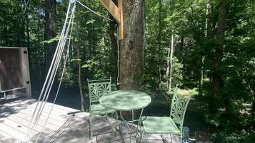 A wooden deck with a swing set, two green chairs, and a table.