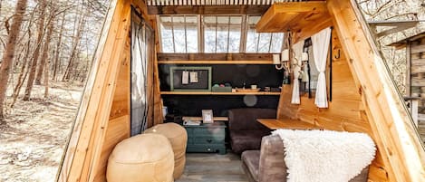 Interior de una cabaña de madera con sofá, reposapiés y una pequeña mesa.