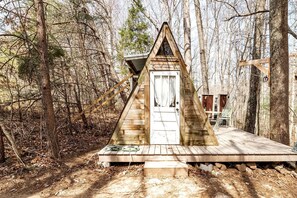 Une cabane en bois avec un toit triangulaire, une porte blanche et une terrasse en bois.