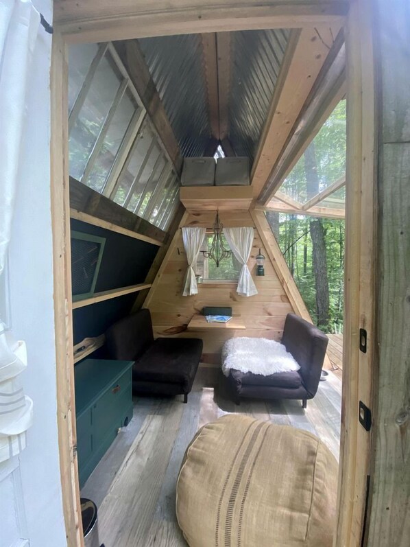 A cozy cabin interior with a sloped ceiling, wooden walls, a sofa, a chair, and a small table. - Off-Grid Experience in Cozy Mini A-Frame in Picturesque Tennessee (Grandview)