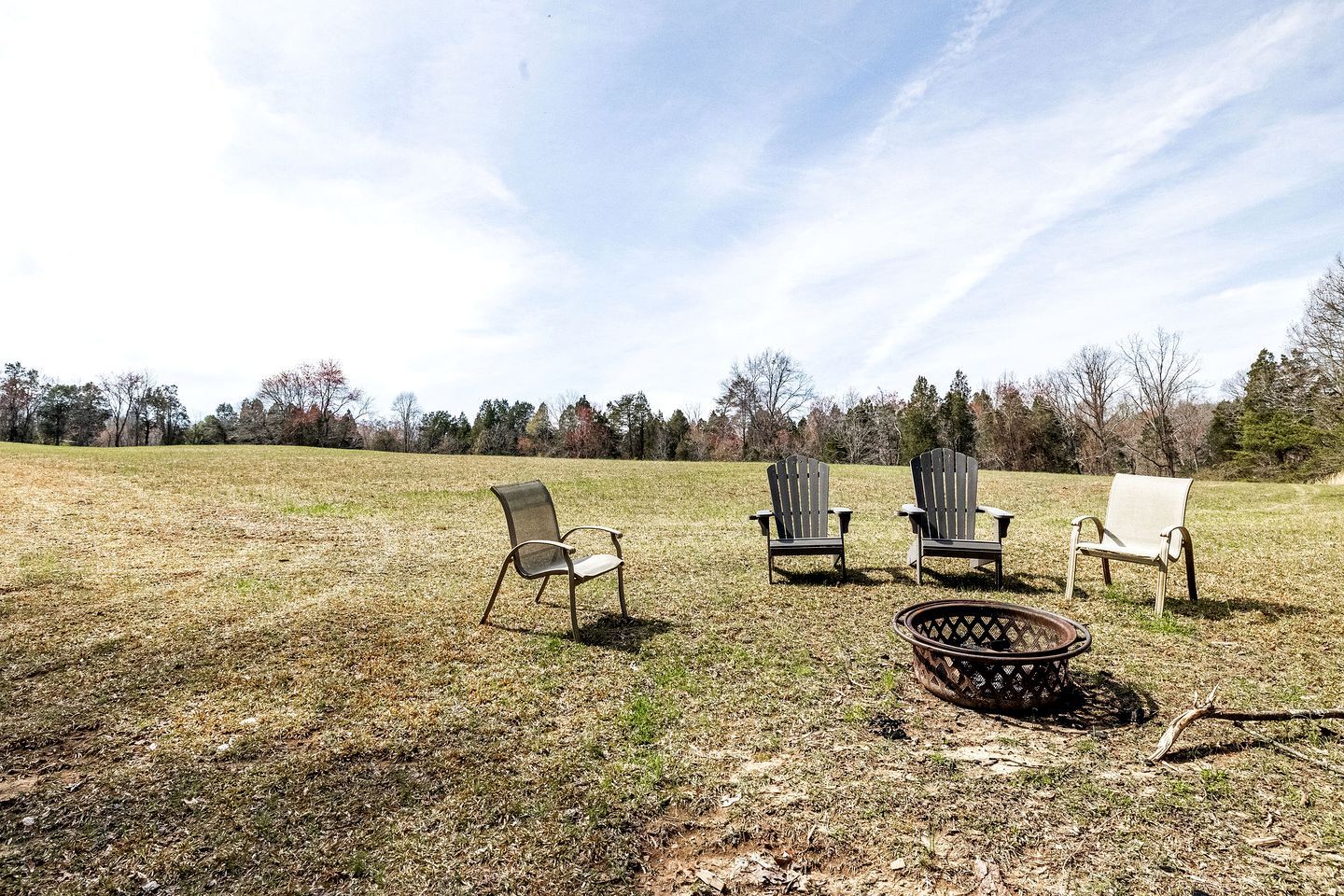 Un campo abierto cubierto de césped con tres sillas Adirondack y un brasero.